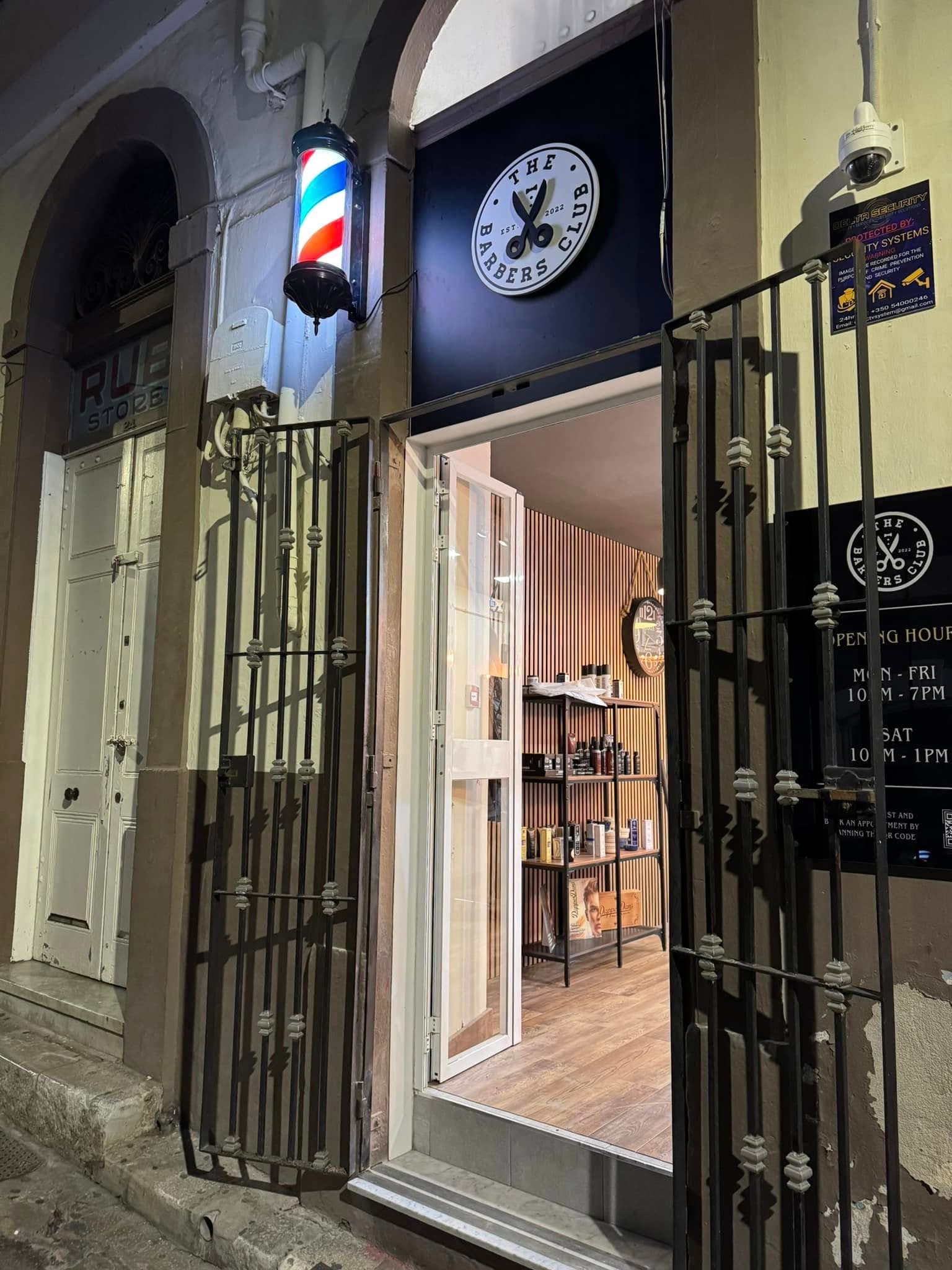 The Barbers Club shopfront on City Mill Lane at night, lit barber pole beside the open door