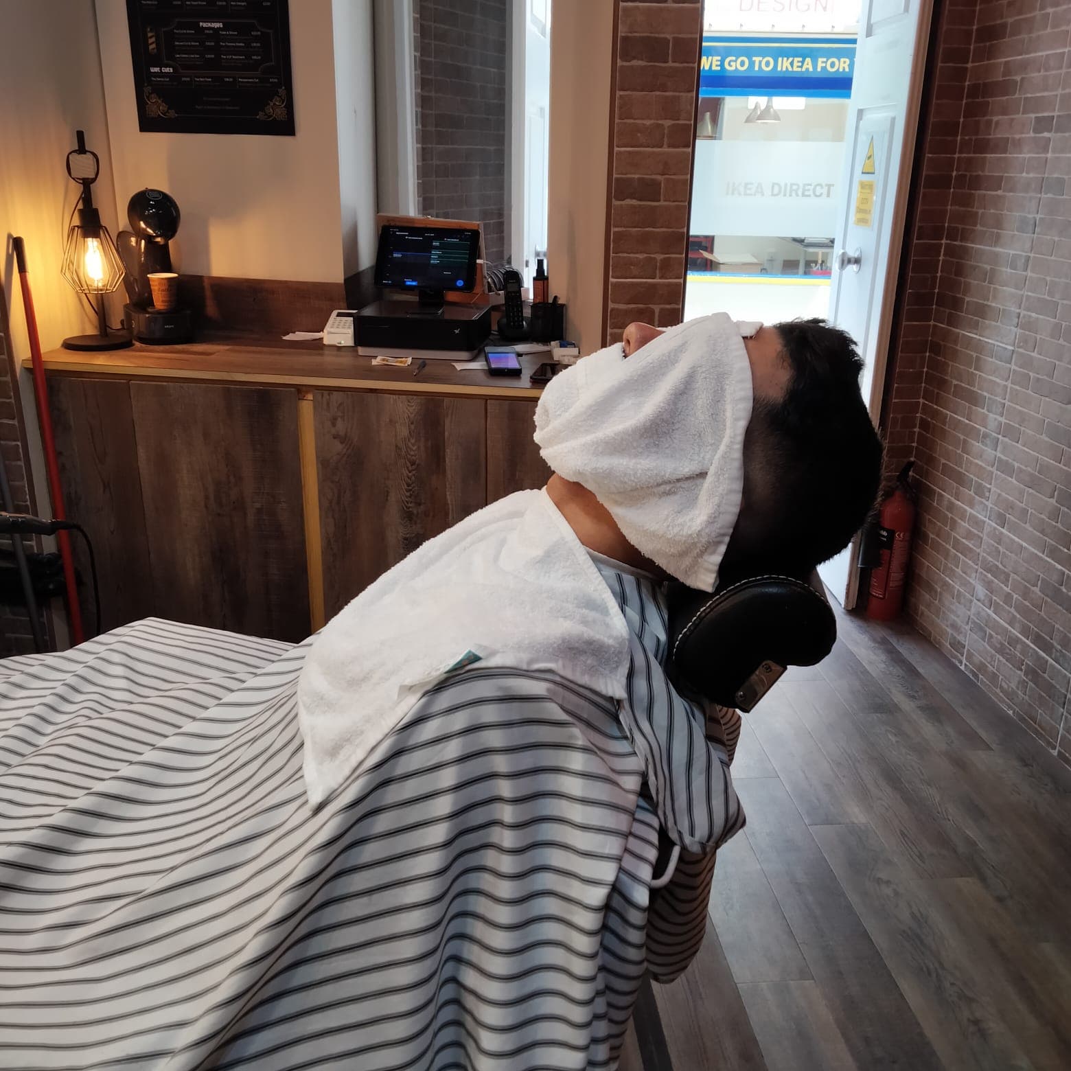 A client reclined in the chair with a hot towel over the face