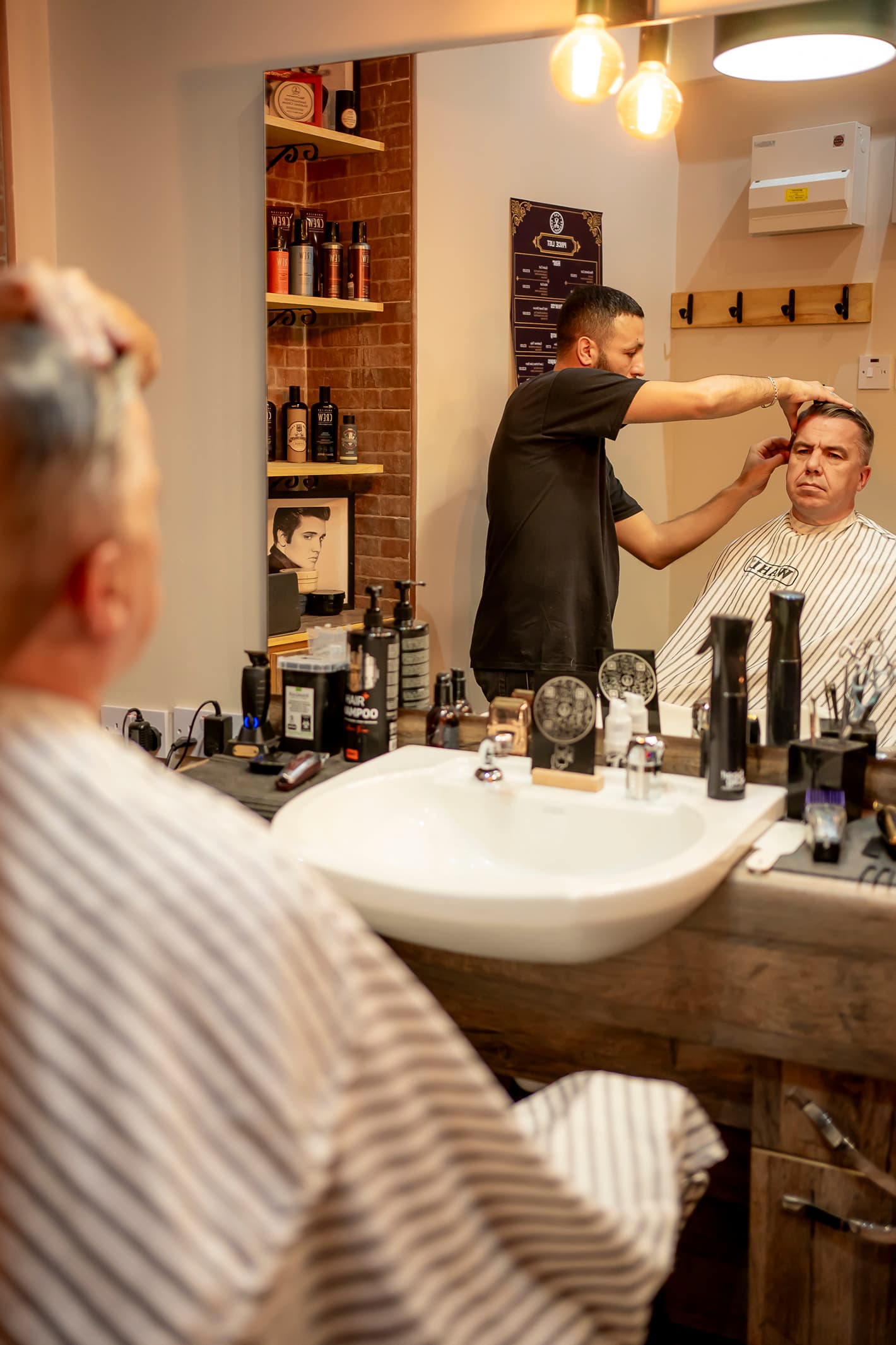 A barber cutting a client's hair in the front chair at The Barbers Club